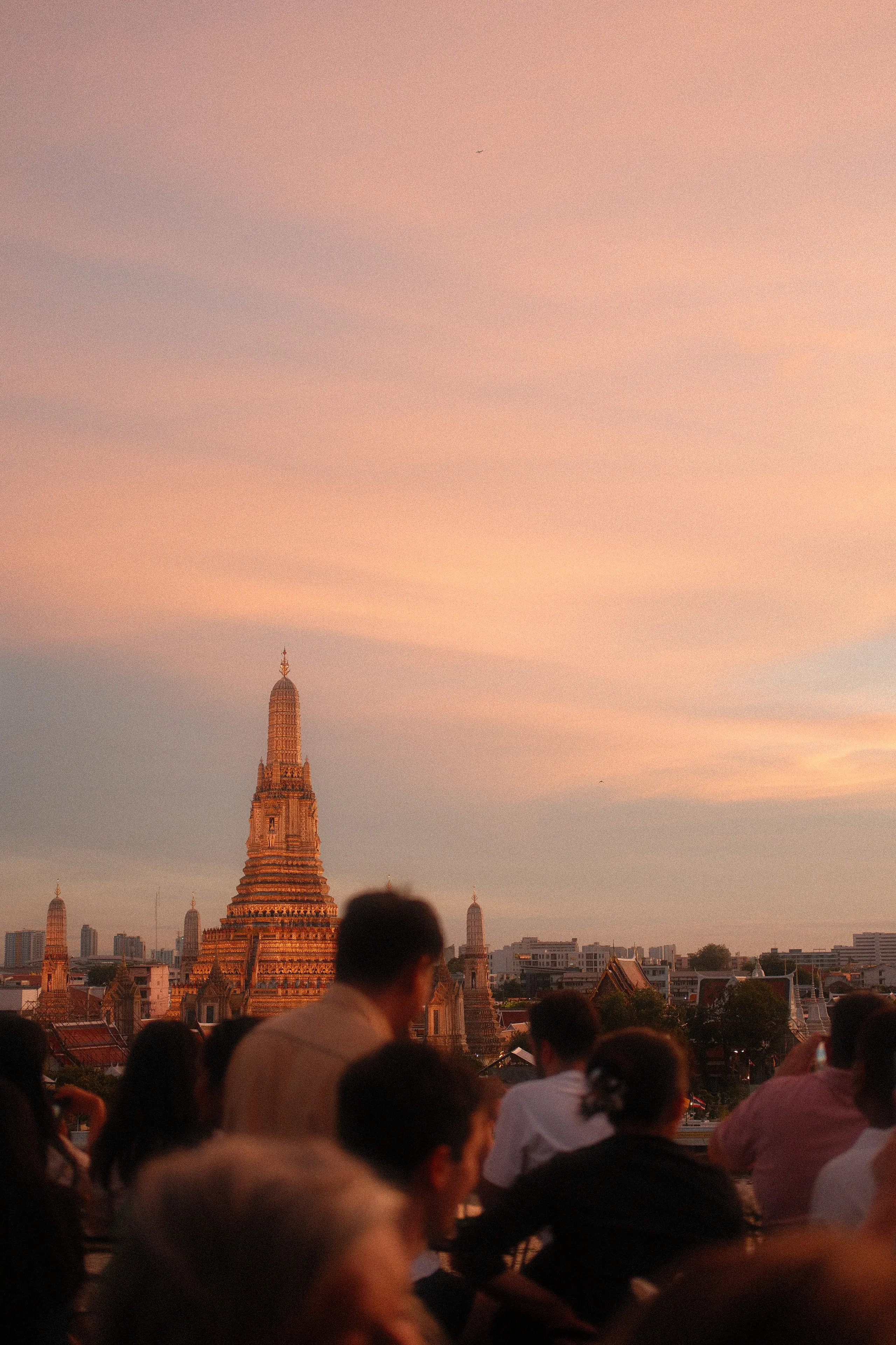 Wat Arun lit at sunset above a crowd watching from across the river