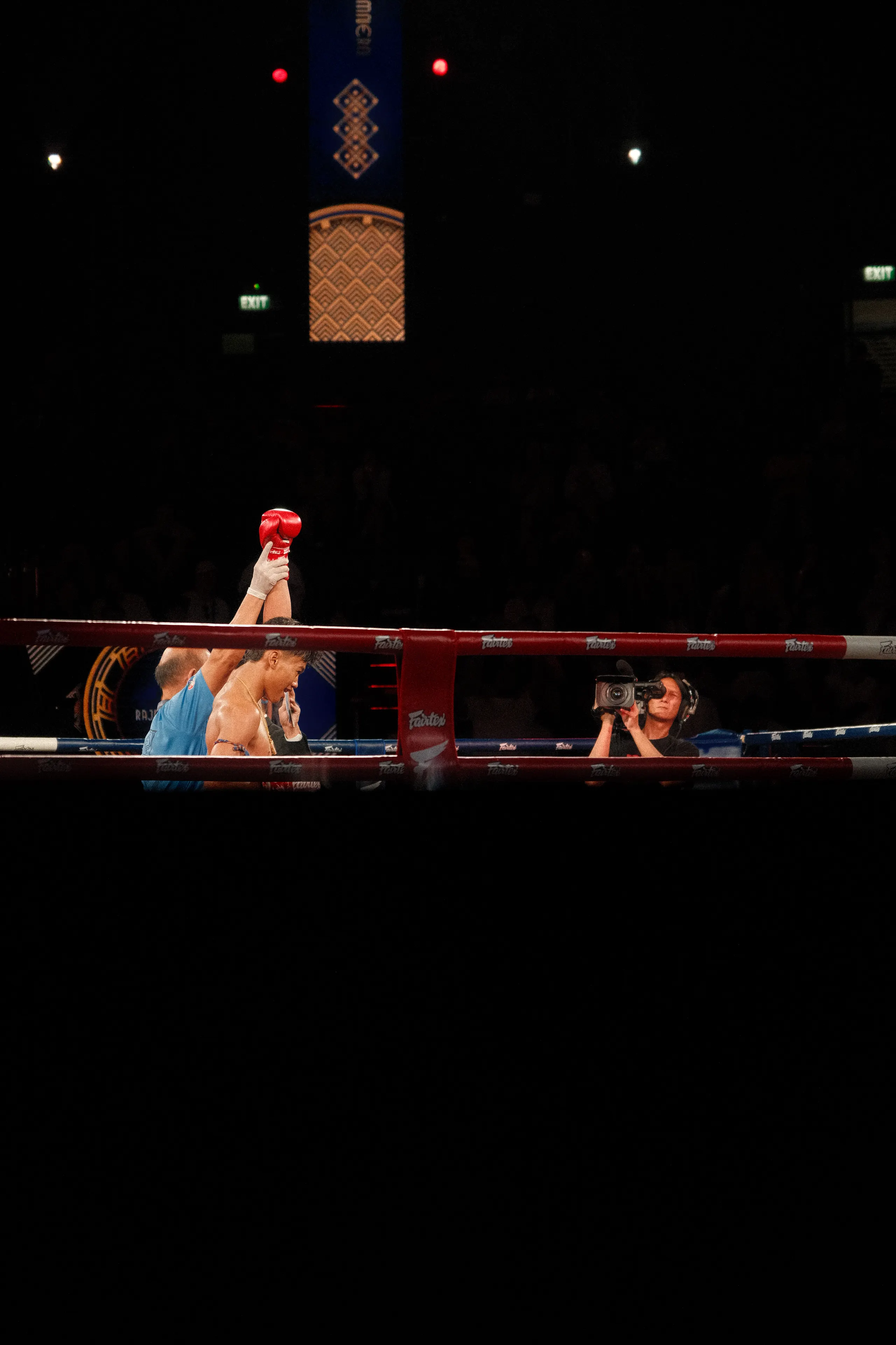 A Muay Thai fighter's arm raised in victory as a camera operator films