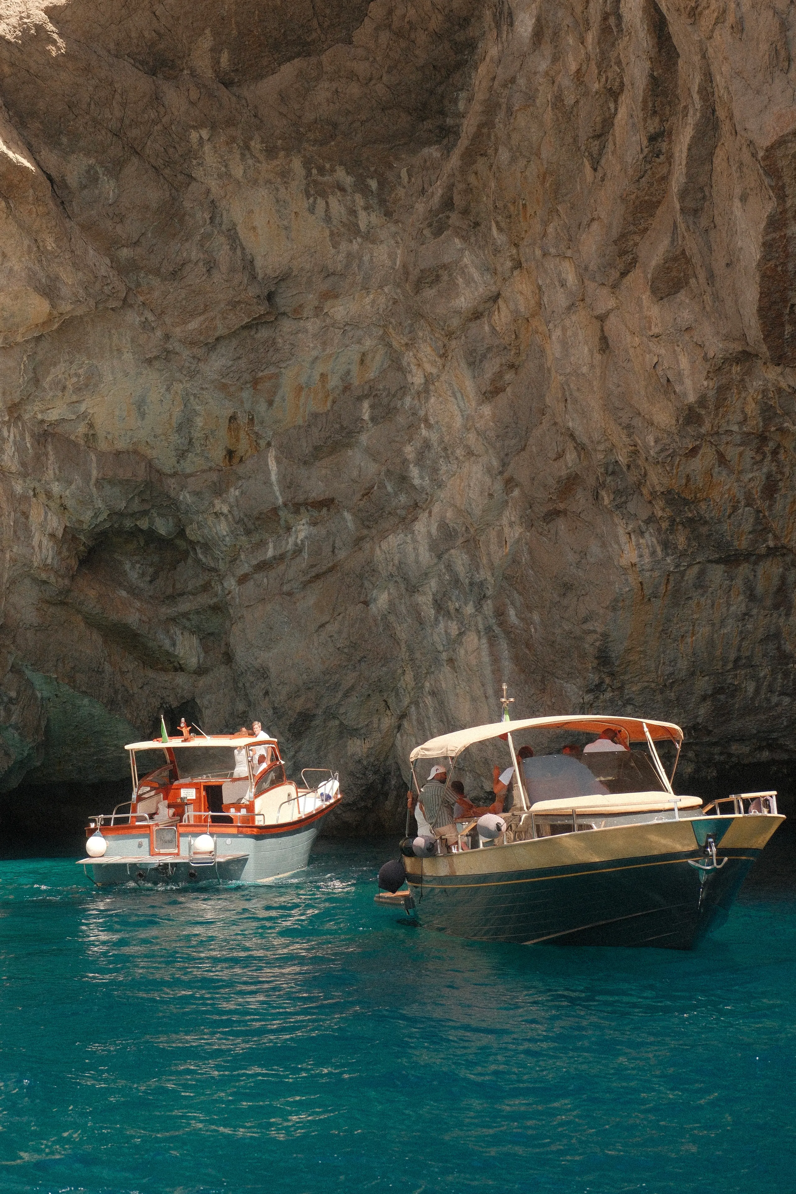 Two boats moored beneath limestone cliffs in turquoise water off Capri