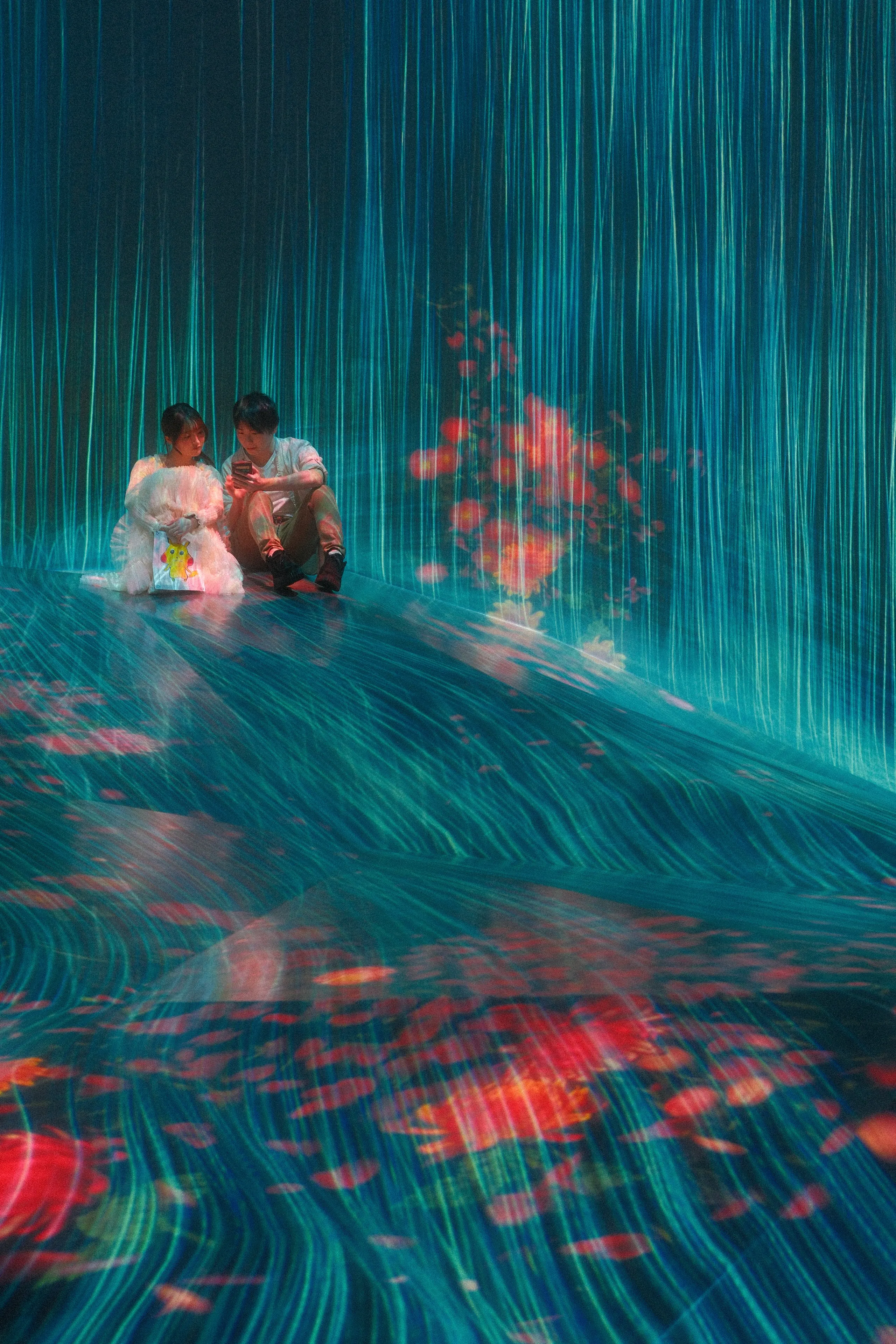 Two people sitting in a stream of projected light at teamLab