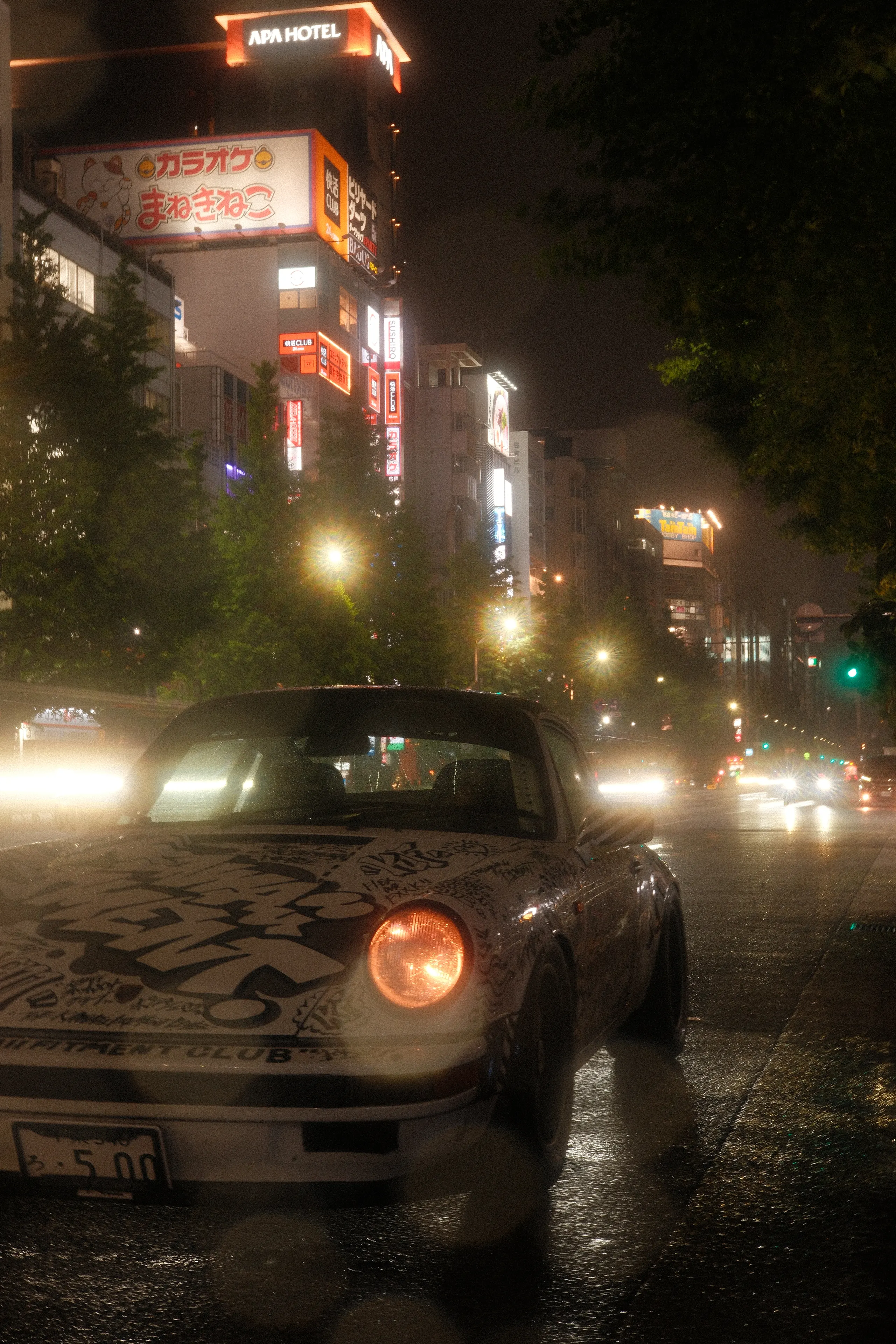 A wrapped classic Porsche on a wet street at night
