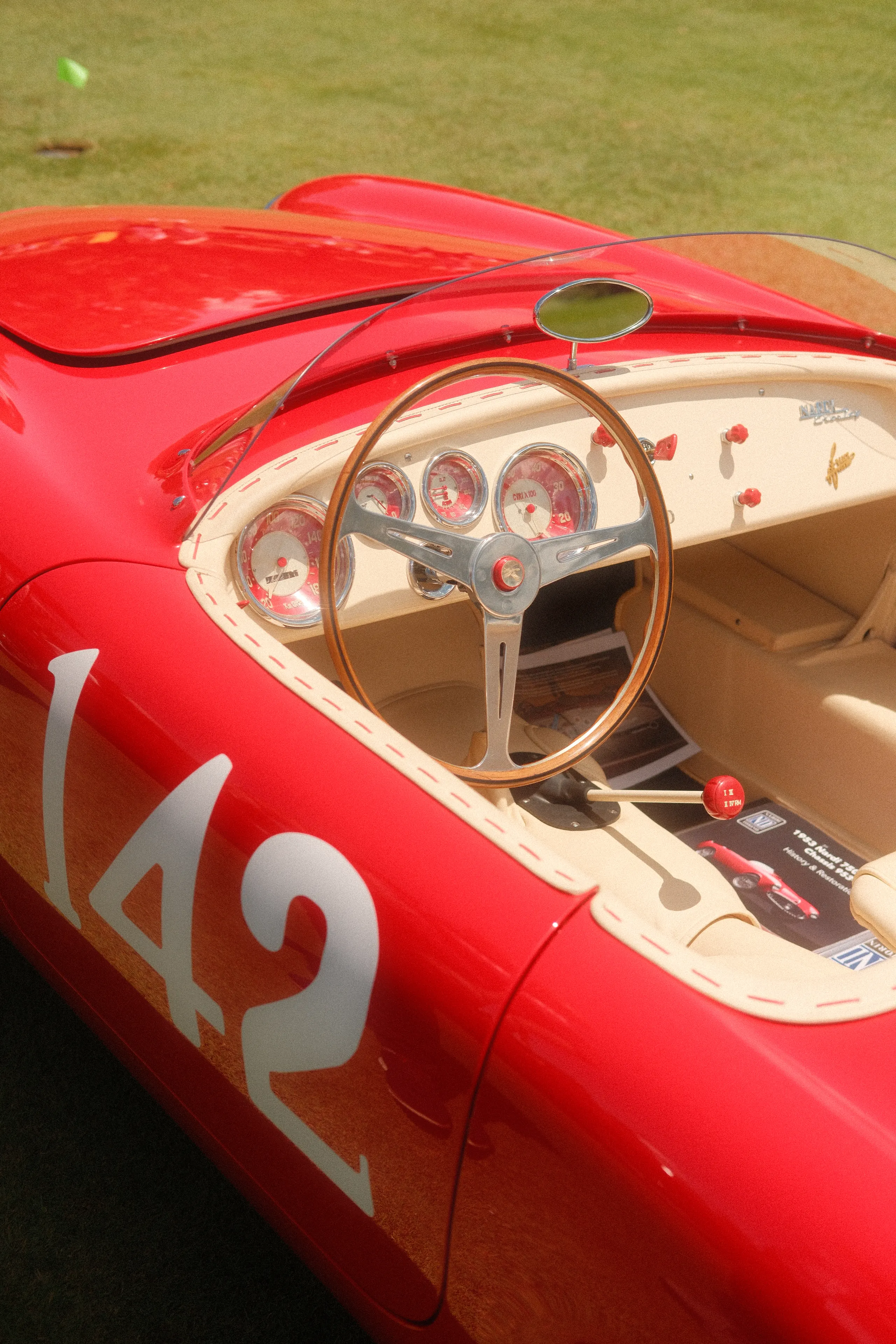 A red racing barchetta numbered 142, its wood-rimmed wheel inside