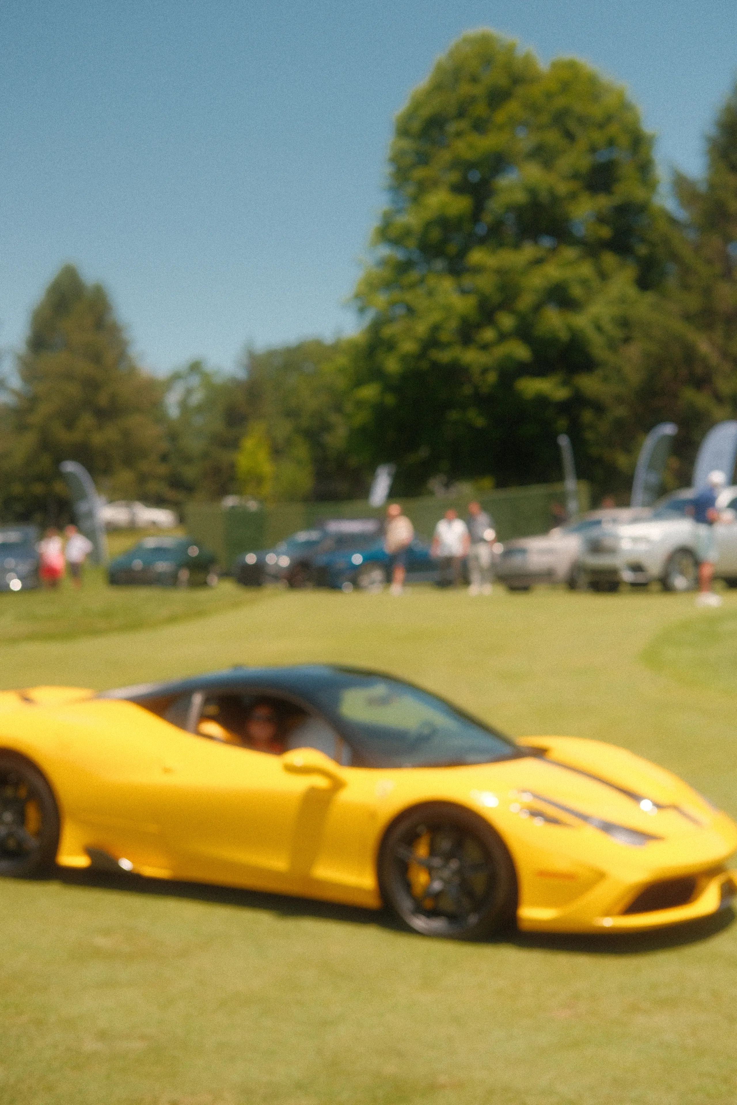 A yellow Ferrari on a field of parked cars
