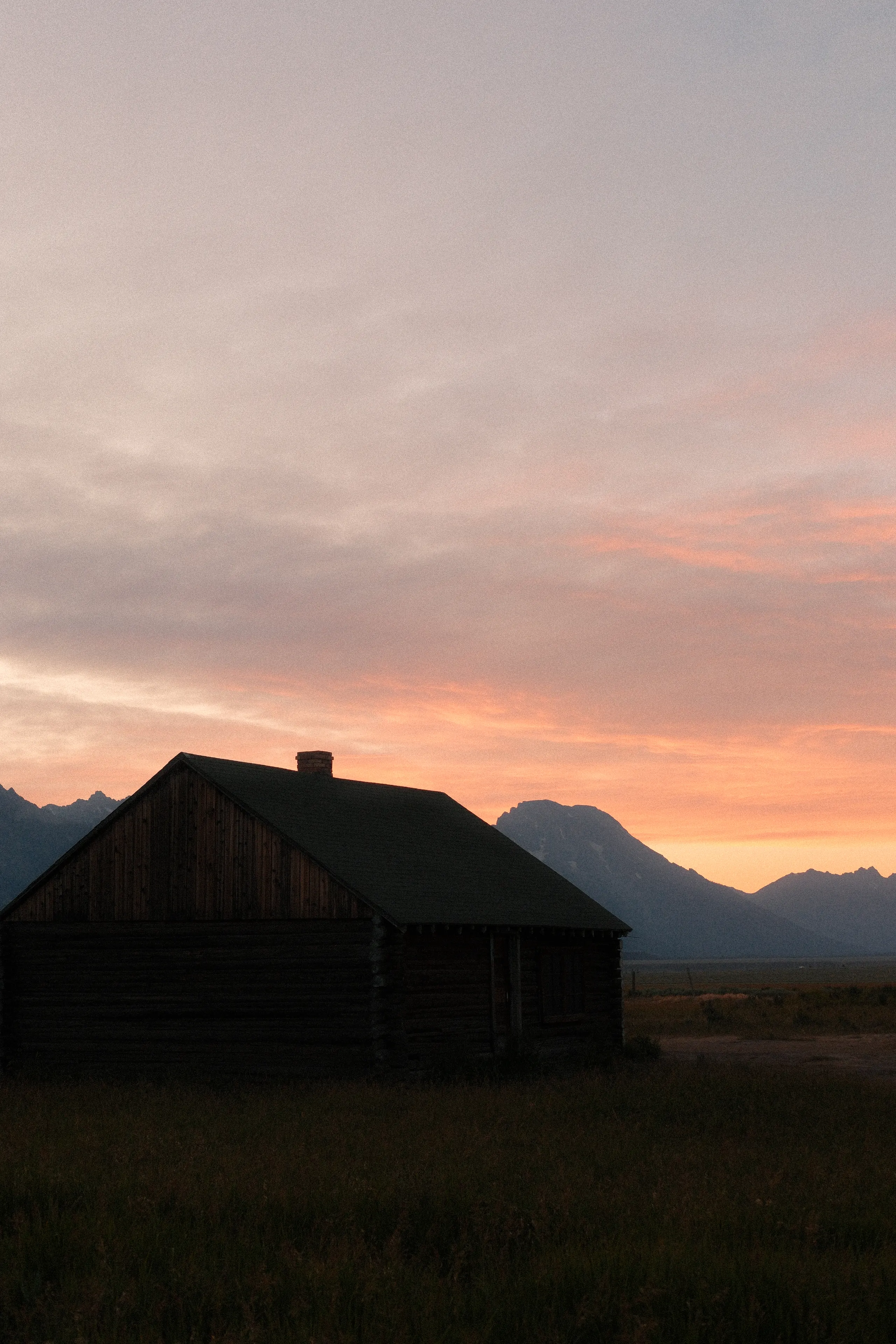 A wooden barn at dusk under a soft pink sky